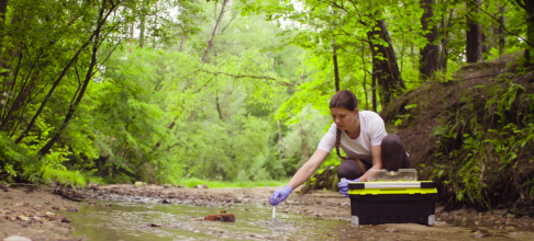 Woman kneeling in a stream taking a sample of the water. 