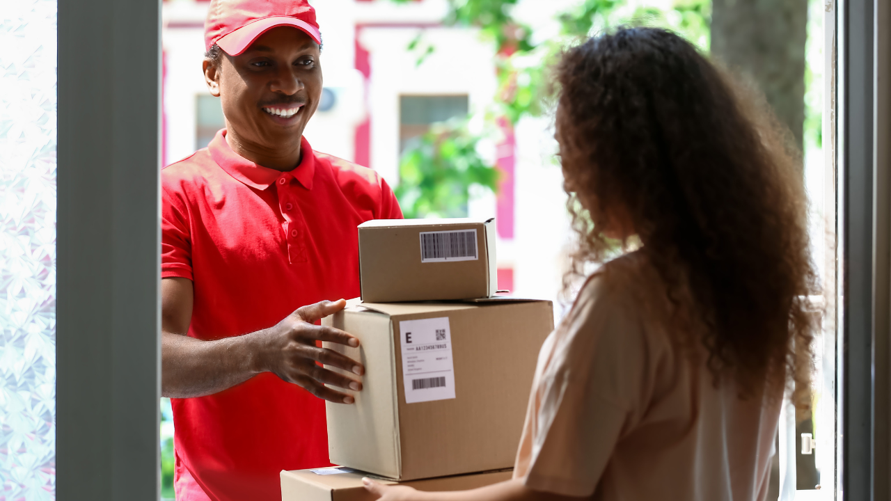 Delivery driver handing parcel across to person standing in doorway.