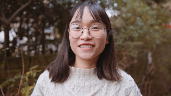 A woman with round glasses stood outside and smiling.