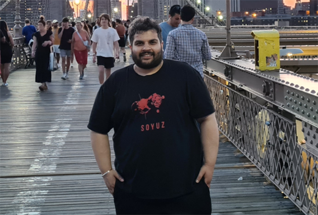 A man standing on a busy bridge in front of city buildings and a sunset.