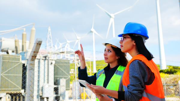 Two women wearing hi-vis jackets looking at wind turbines.