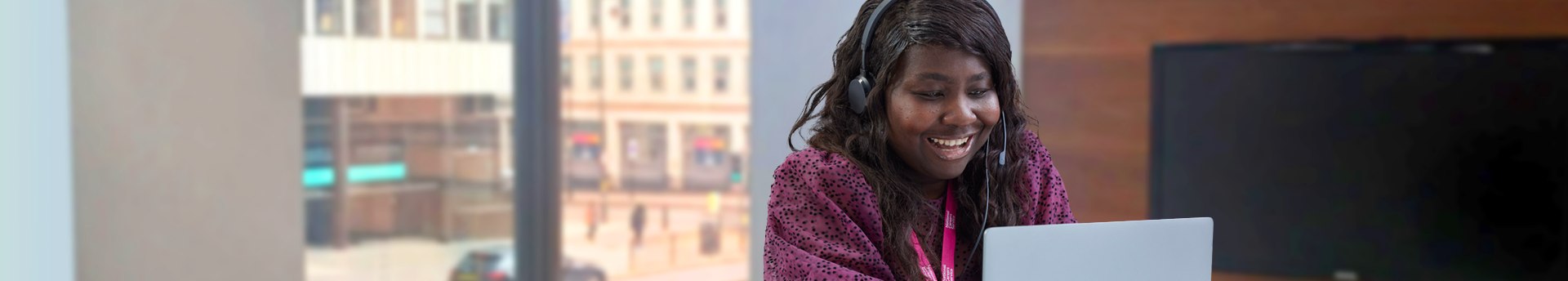 Woman sat at a laptop and wearing a headset in an office. 