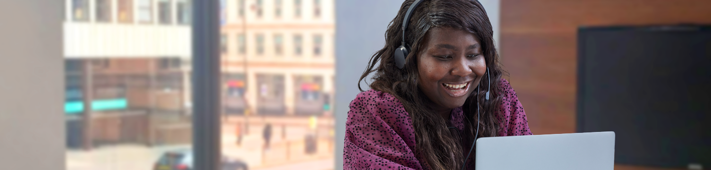 Woman sat at a laptop and wearing a headset in an office. 