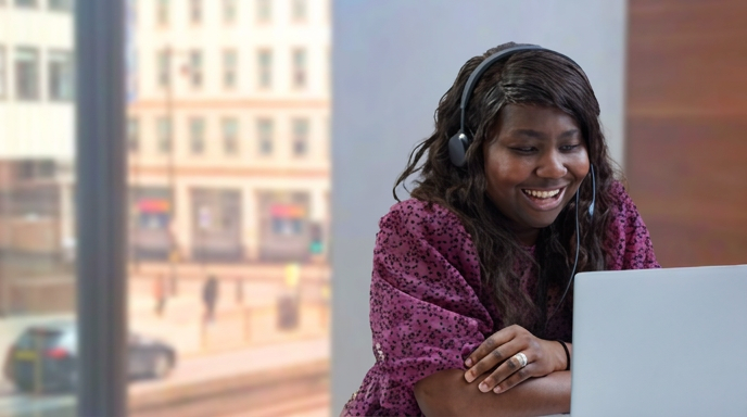 Woman sat at a laptop and wearing a headset in an office. 