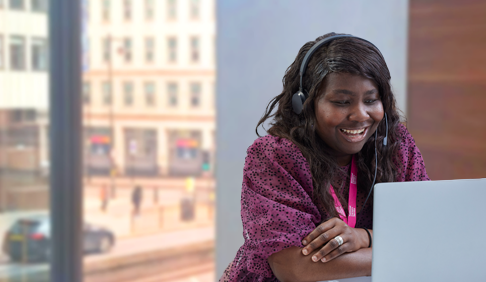 Woman sat at a laptop and wearing a headset in an office. 