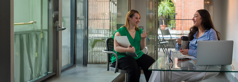 Two women chatting at desk.