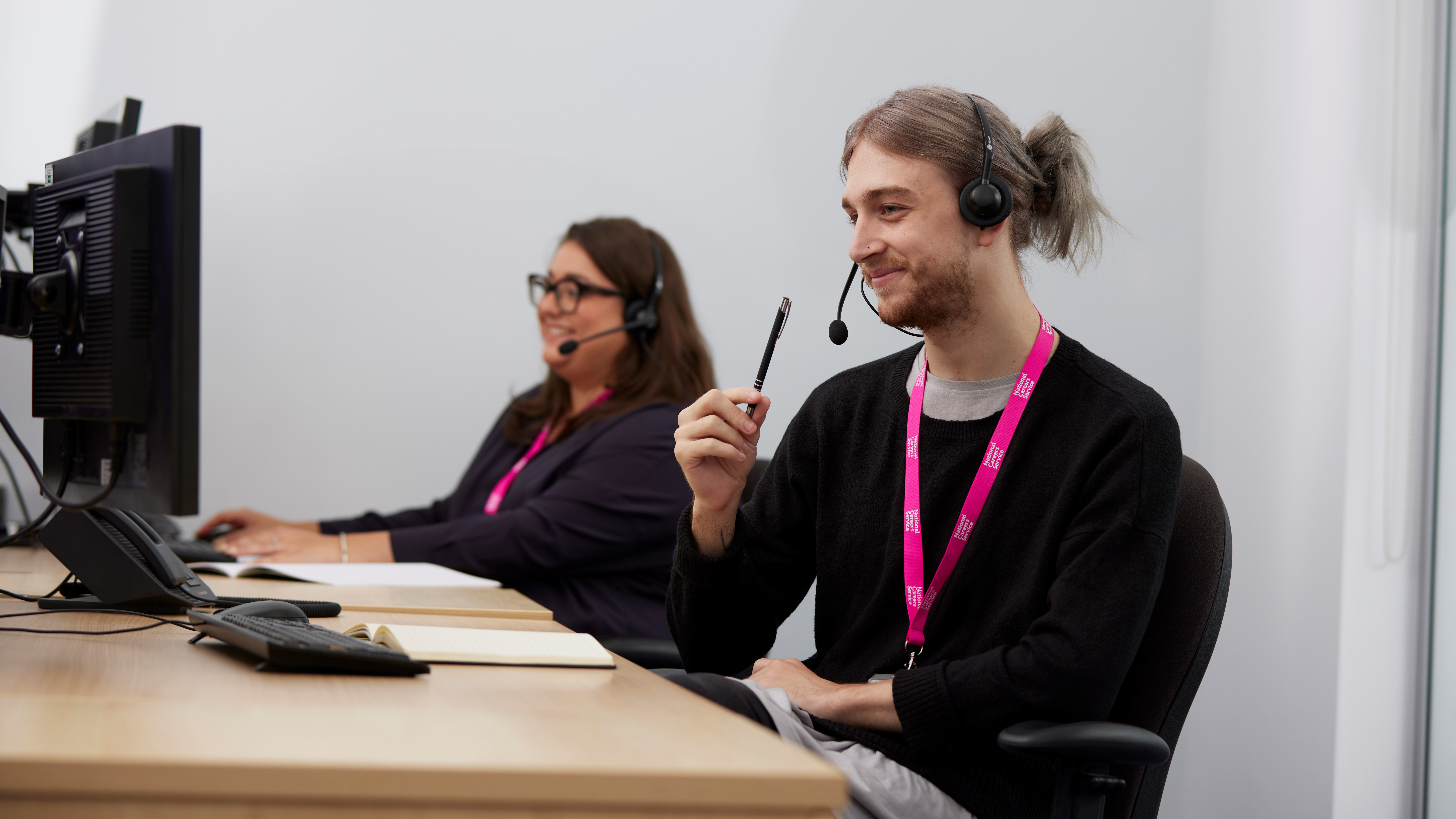 A man and a woman working at computers with headsets on.