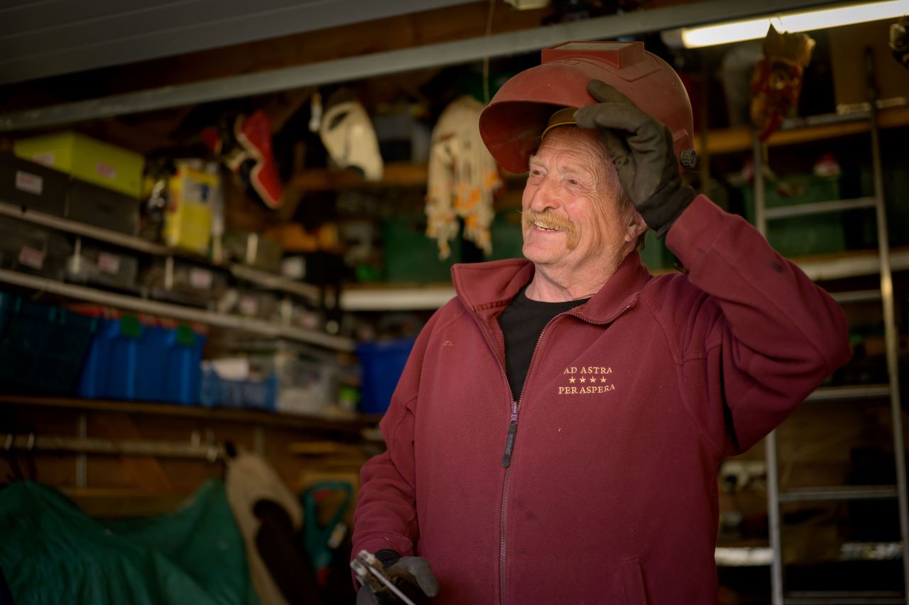 A man in overalls lifting his helment up and smiling