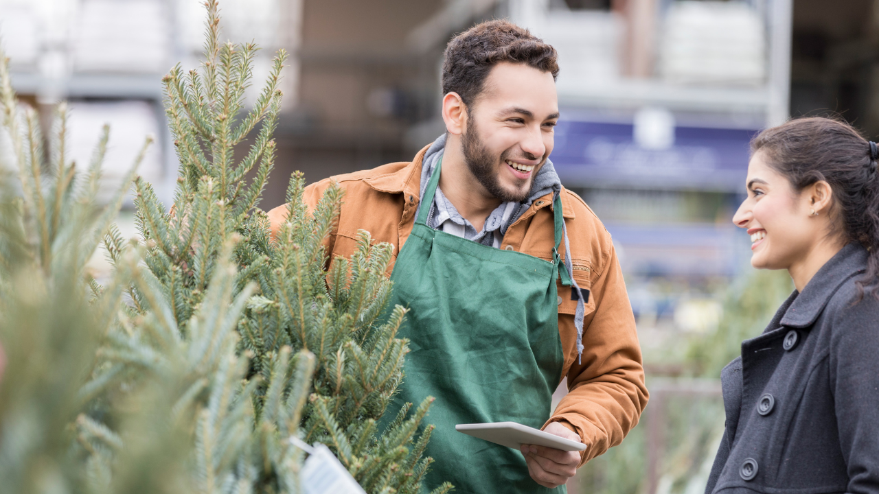 A man selling a Christmas tree to a person.