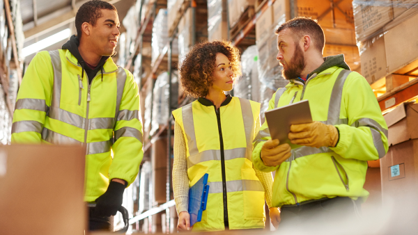 3 people in high visibility jackets standing in a warehouse. 