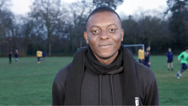 A man stood on a football field with football players in the background.