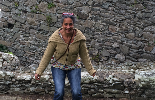 A woman crouching and smiling in front of a brick wall.