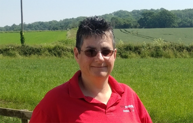 A middle aged woman smiling in front of fields and trees.
